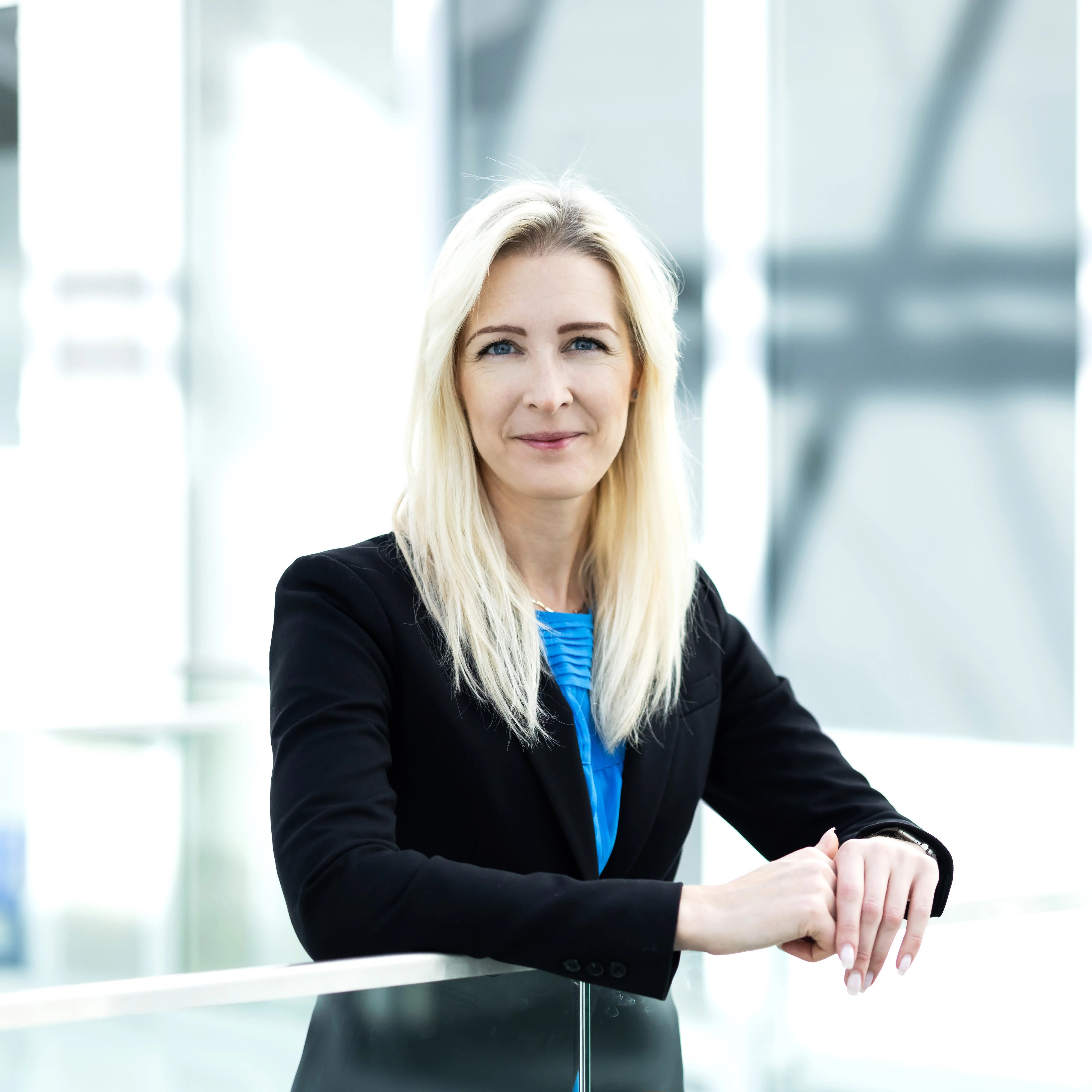 Portrait of Justina Banionienė, Project Manager at the KTU Lifelong Learning Centre, photographed in the interior of Kaunas University of Technology&rsquo;s Santaka Valley. A woman with shoulder-length light hair and no glasses looks into the camera with a gentle smile. She is wearing a dark blazer and a light blue shirt.