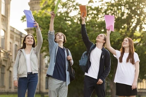 Džiaugsmingi jaunuoliai su pakeltais spalvotais segtuvais švenčia mokymosi pasiekimus. Įkvepianti mokymosi motyvacija ir jaunimo įsitraukimas.